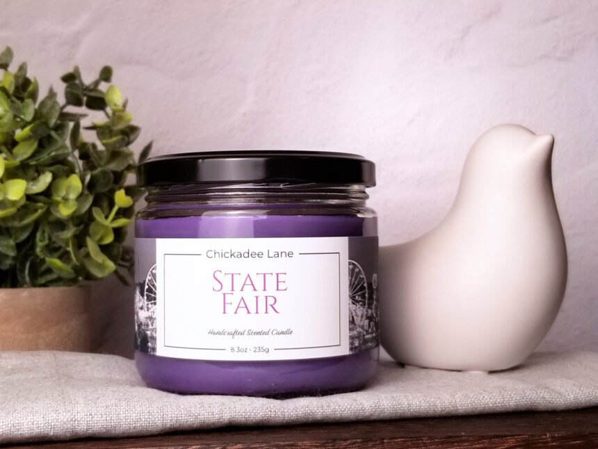 State Fair candle sitting on a shelf between a plant and a porcelain bird.