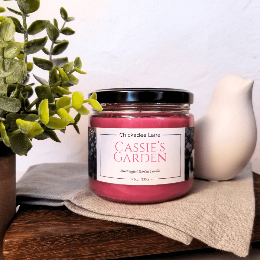 Cassie's Garden candle sitting on a shelf between a plant and a porcelain bird.