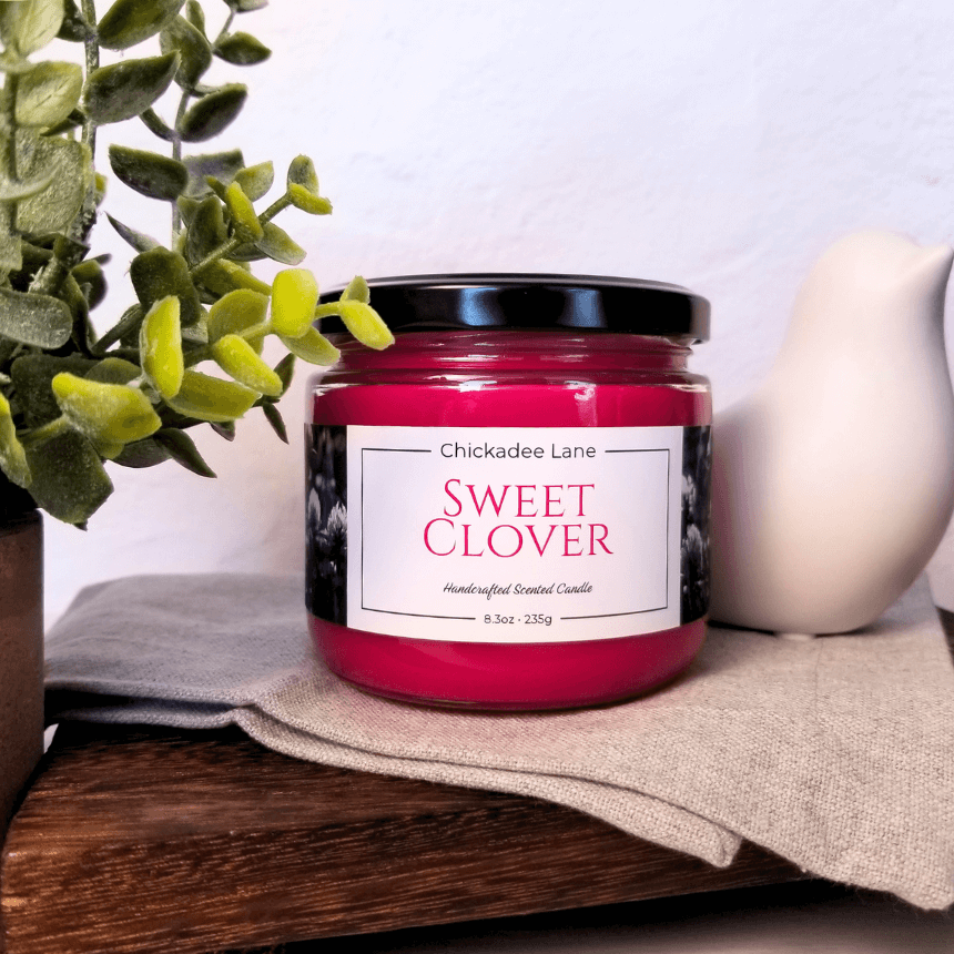 Sweet Clover candle sitting on a shelf between a plant and a porcelain bird.