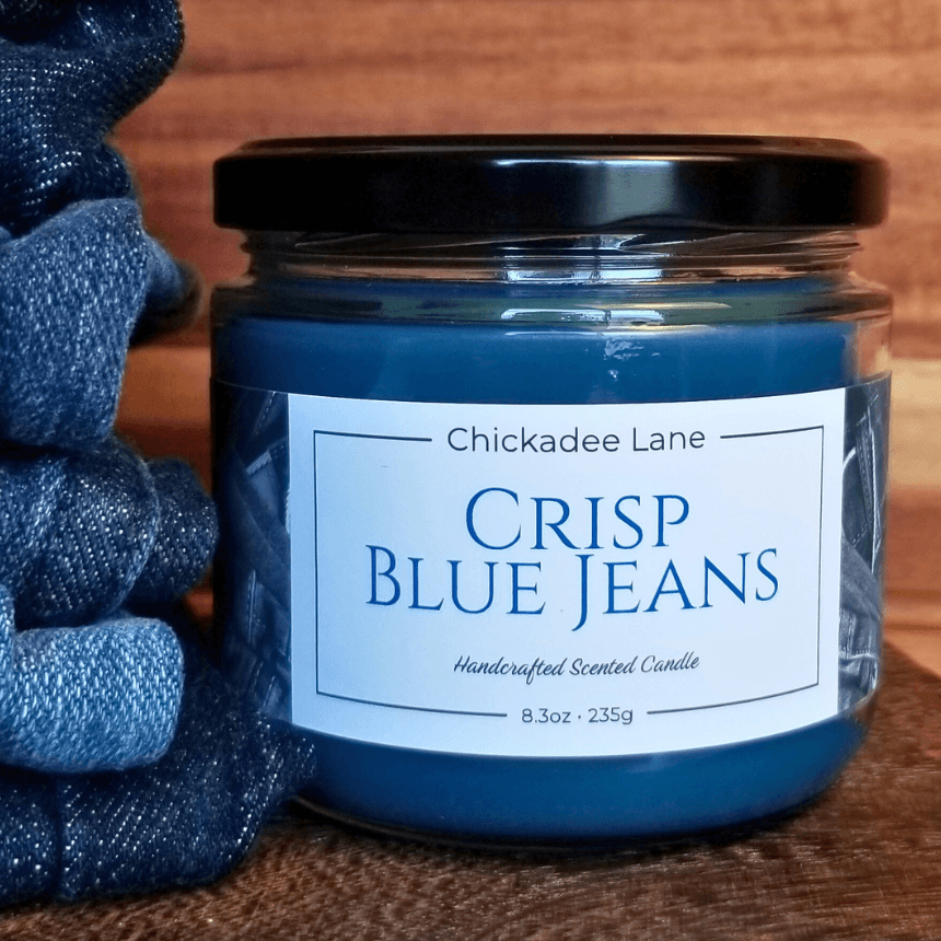 Crisp Blue Jeans candle sitting next to a stack of folded blue jeans.