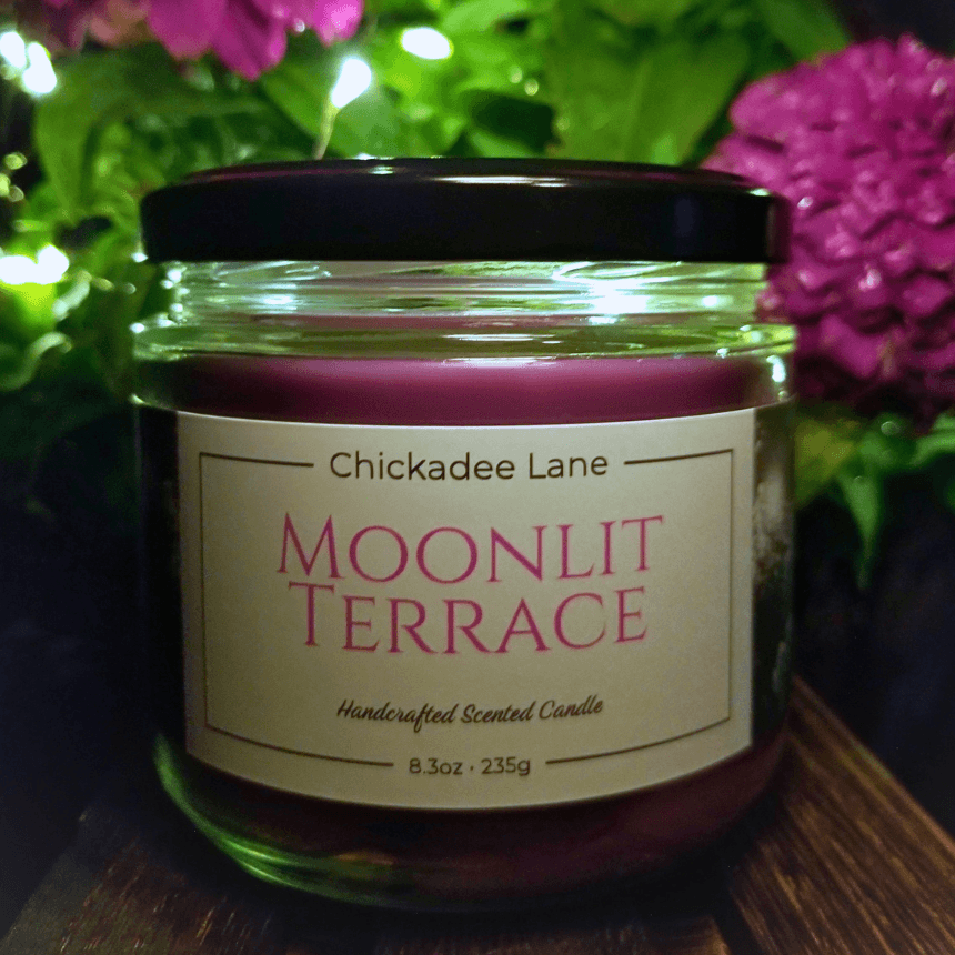 Moonlit Terrace candle sitting in front of a blooming plant at night.