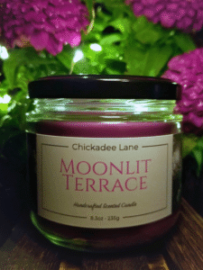 Moonlit Terrace summer scents candle in front of purple flowers at night.