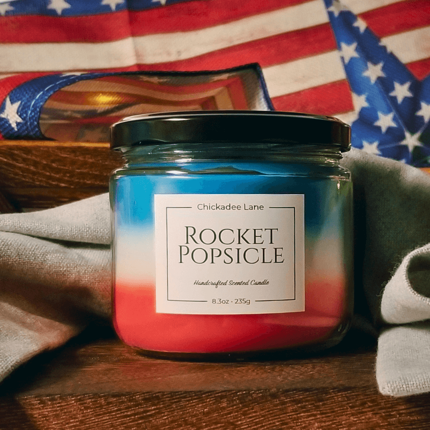 Rocket Popsicle candle sitting on a wooden shelf in front of a patriotic red whit and blue banner.